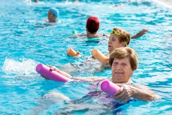 Close up portrait of senior woman doing body exercise with friends at aqua gym session in outdoor pool.