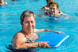 Close up portrait of senior woman doing water exercise with kicking board in outdoor pool.