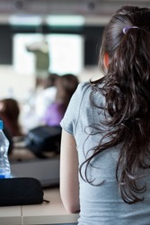 young pretty female college student sitting in a classroom full of students during class