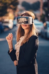 Confident young beautiful girl gesture testing virtual reality 3D video glasses VR headset dressed in a office outfit impressed by augmented reality on the street and beautiful autumn sun light colors