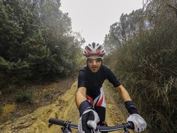 POV, Original point of view. Happy Young man on bicycle take a selfie with action cam and selfie stick. Training on mountain bike on a mountainous road in a rainy day