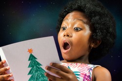 Close up face shot of little african girl reading a christmas card with surprised face expression.Excited kid with mouth open against galaxy star background.