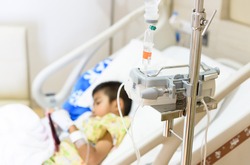 Close up IV set and blurry illness asian boy sleeping on hospital bed.Medical equipment concept.