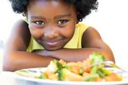 Close up face shot of cute African girl in front of healthy vegetable dish. Isolated on white.