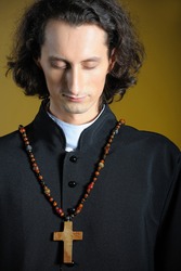 conceptual portrait of Praying priest with wooden cross praying. yellow background