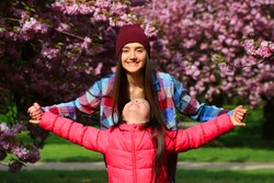 Happy beautiful young woman with girl in blossom park with trees and flowers.
