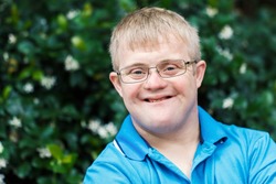Close up face shot of friendly young man with down syndrome against outdoor green background.