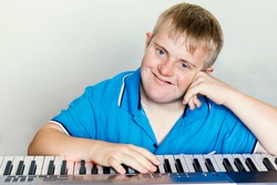 Close up indoor studio portrait of young pianist with down syndrome next to piano keyboard.
