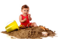 A baby girl with sand toys and shells making faces after tasting the sand she's sitting in. Isolated on white.