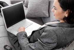 Young businesswoman sitting on sofa, working with laptop computer. Isolated on white background, overhead view.