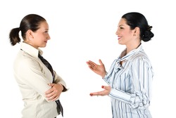 Two cheerful businesswoman have a conversation,the brunette woman explaining something and gesturing with hands while the other listen her very attentive
