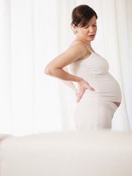 italian 7 months pregnant woman massaging her back. Vertical shape, side view, copy space