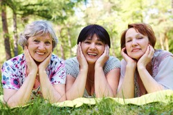 Portrait of three aged women resting on grass and looking at camera with smiles