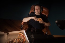 Man at home eating a slice of pizza and social networking with a lpc computer late at night. Unhealthy Lifestyle.