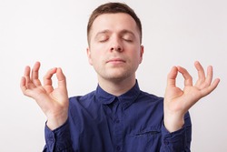 Young man in a blue shirt, breathing deeply, trying to calm down. Fingers together, his eyes covered