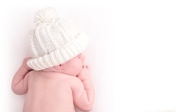 A newborn baby is wearing a white hat and laying down sleeping on a white isolated background. Use the photo to represent life, parenting or childhood.