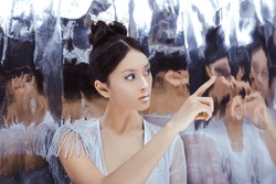 Portrait of futuristic young woman touching reflection in mirror. Reflection of our mind and soul concept. Beautiful young multi-racial asian caucasian model cyber girl in silver urban clothes with