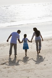 Rear view of Hispanic family with 9 year old girl holding hands walking on beach
