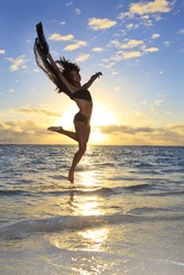 beautiful black female dancer leaping in the air over the ocean at sunrise in the tropics