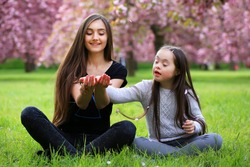 Happy beautiful young woman with girl in blossom park with trees and flowers.