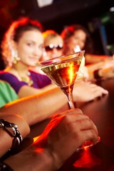 Glass of martini on background of row of smart teens in the nightclub