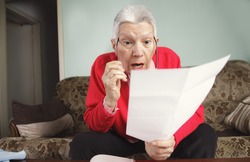 Senior old woman shocked with the bills she receives, appalled and surprised