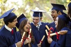 Graduating students smiling and laughing with diplomas; trees in background