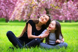 Happy beautiful young woman with girl in blossom park with trees and flowers.