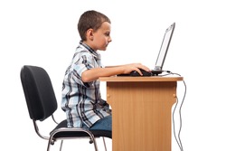 Cute schoolboy sitting at his laptop doing homework or playing, isolated on white background