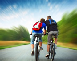 Two riders with backpacks on bikes riding on an rural asphalt roar. Motion blurred