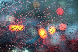 Defocussed traffic viewed through a car windscreen covered in rain, focus on raindrops