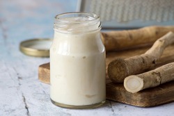 The root of horseradish, a jar with seasoning and a metal grater on old wooden table.