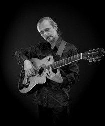 An elderly gray-haired male musician with long hair with a guitar in his hands playing and posing on a black background in a blue scenic light