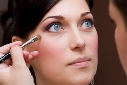 make up artist makeing a colour correction with an brush to the beautiful young lady bride