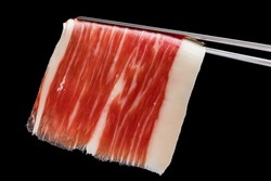 Extreme macro close up of cut piece of cured Spanish bellota pork ham on tweezers.