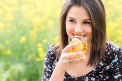 Close up portrait of attractive girl drinking ice tea outdoors against yellow flower background.