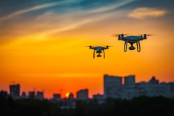 Two drone quad copters with high resolution digital camera flying aerial over spectacular sunset orange sky. Cityscape silhouette with sun goes down in the background.Vehicle at sundown and copy space