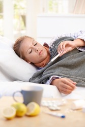 Young female at home having flu, feeling bad, taking her temperature in bed.?