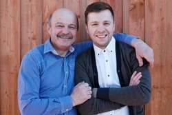 Family portrait. Father-in-law embraces the son-in-law. They are smiling at the camera.