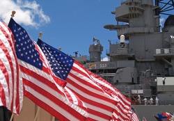 US flags flying beside the Battleship Missouri in Pearl Harbor, Honolulu, Oahu, Hawaii with 4 sailors walking on deck.