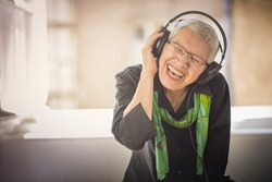Senior old woman listening to her favourite music through big headphones, enjoying the rich sound