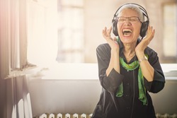 Senior old woman listening to her favourite music through big headphones, enjoying the rich sound