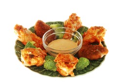 Closeup of spicy buffalo chicken wings and jalapeno pepper poppers with spicy dip and broccoli sprigs isolated on green plate with dipping sauce.