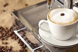 Espresso cup full with coffee beans. In background are more coffee beans visible.