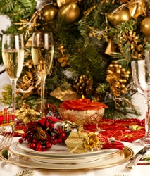 Christmas dinner place setting with Christmas table cloth,, plates, knife and fork, small presents, candles, christmas decorations champagne and wine glass, party