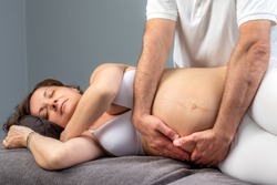 Close up portrait of pregnant woman receiving osteopathic treatment on tummy.