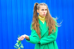 a young girl dressed in a green coat and yellow dress. Pure colors in the photo. girl fun fooling around . against the background of blue wall to show emotions