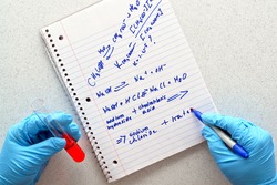 Scientist hand holding a test tube with red liquid and writing chemistry formulas on a notebook during an experiment in a science research lab