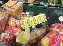 Europe UK Bedfordshire Bedford July 2017. Supermarket food in green crates ready to be reduced in price. Roll of reduced yellow stickers with bar codes in black plastic printing machine.