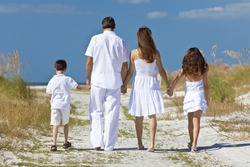 Rear view of mother, father and two children, son and daughter, walking holding hands in the sand of a sunny beach